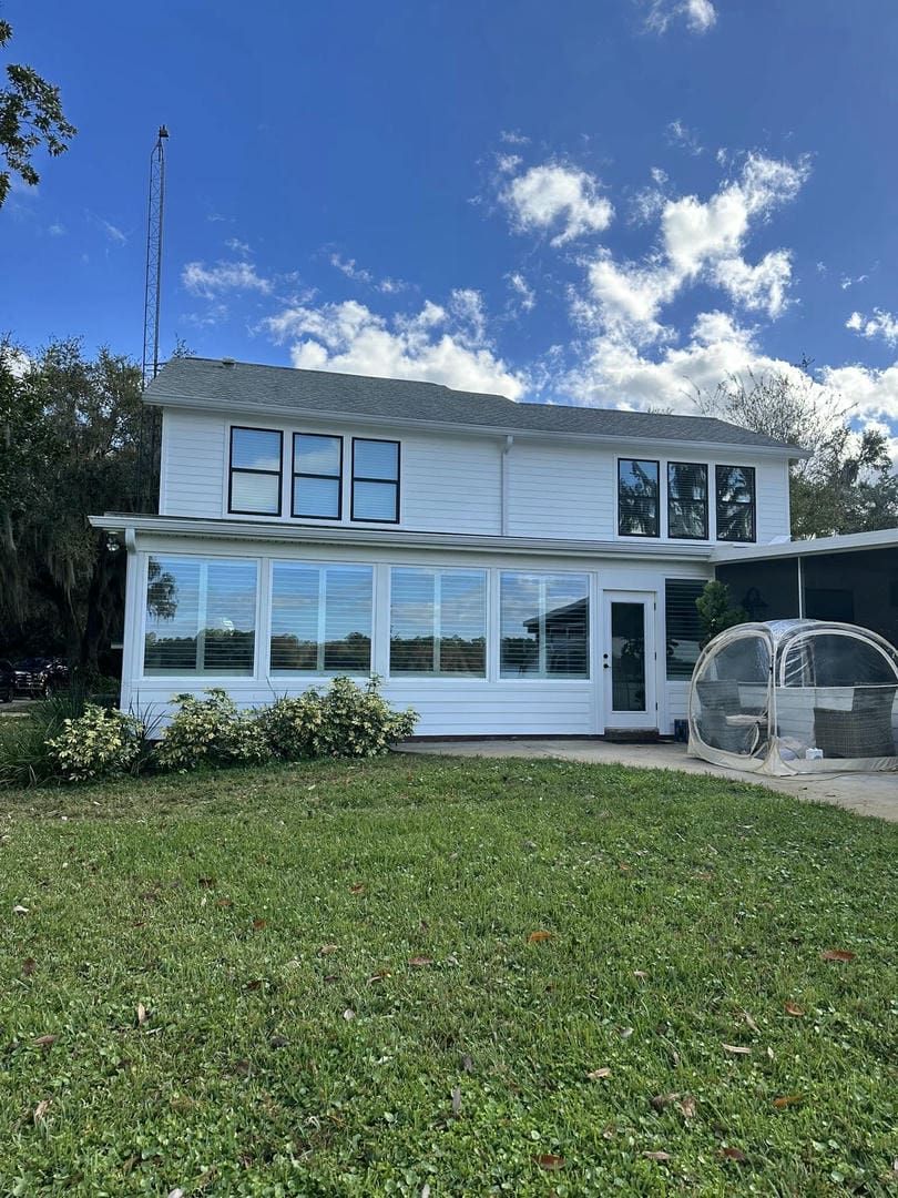 Two-story white house with large windows, set on a green lawn under a blue sky.