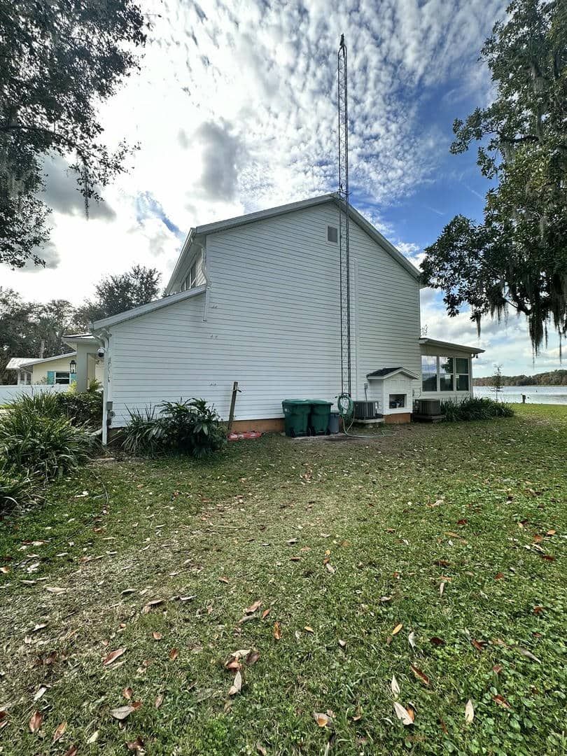 White house with a tall antenna, green grass, and trees under a cloudy sky.