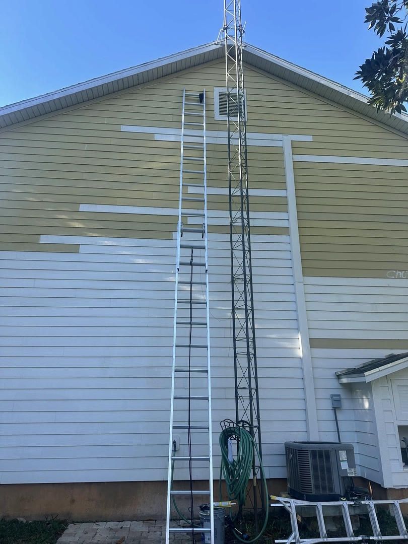 A tall ladder and tower mounted on a house's side. The house has white siding and a beige roof.