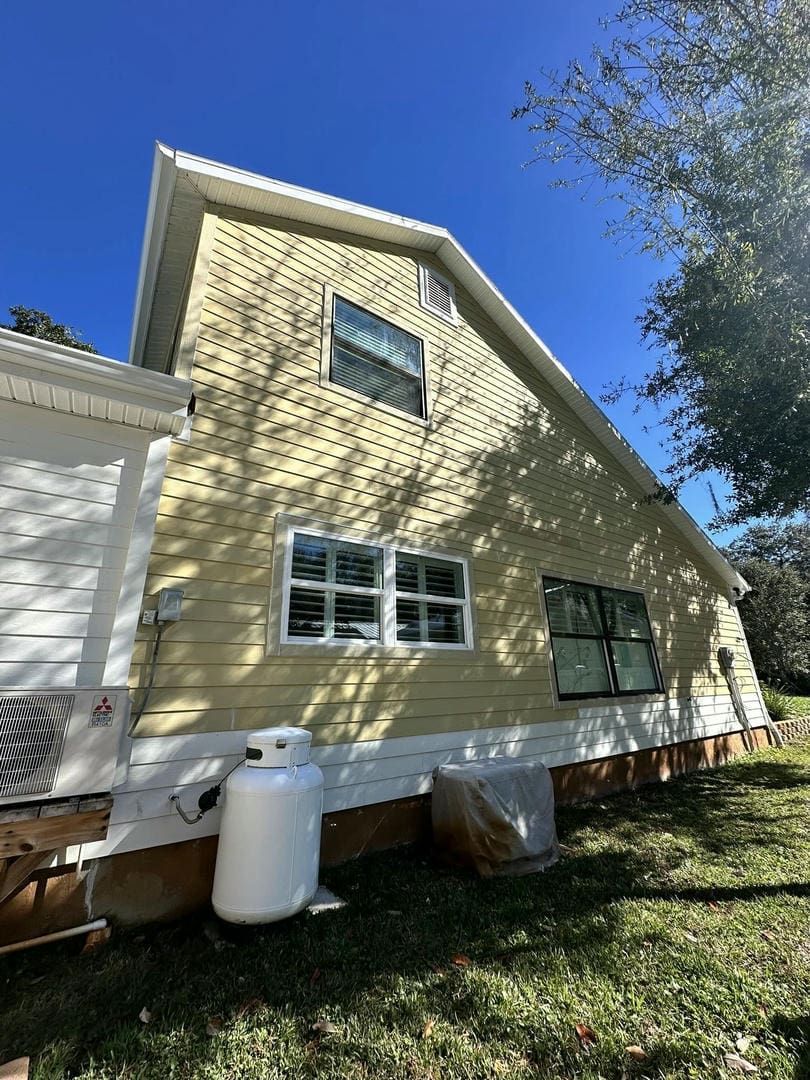 Side view of a yellow house with white trim, windows, and propane tank on a sunny day.