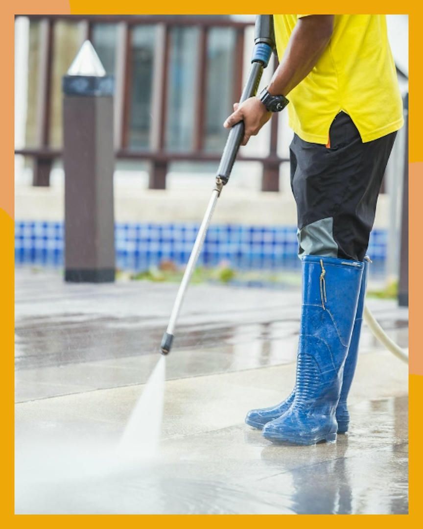 Person pressure washing a concrete surface. Wearing yellow shirt and blue boots. Outside, near a pool.