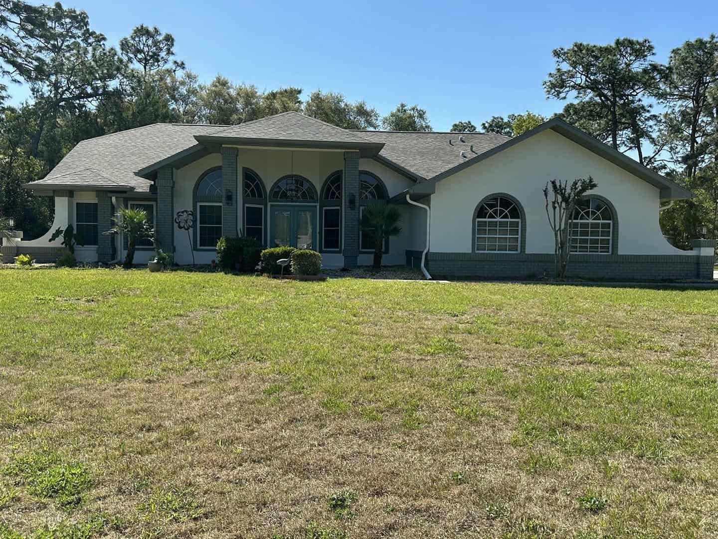 A ranch-style house with arched windows and a gray roof on a green lawn under a blue sky.