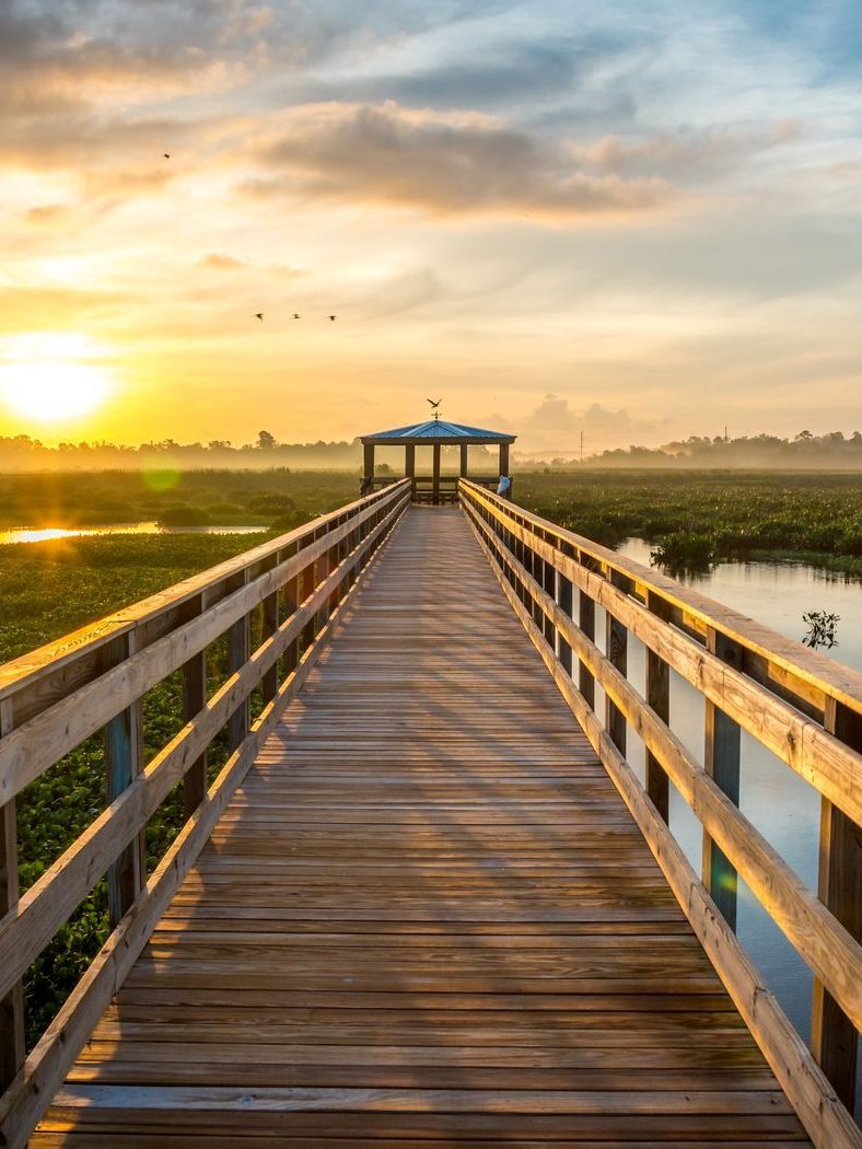 a wooden walkway leading to a gazebo overlooking a body of water at sunset .