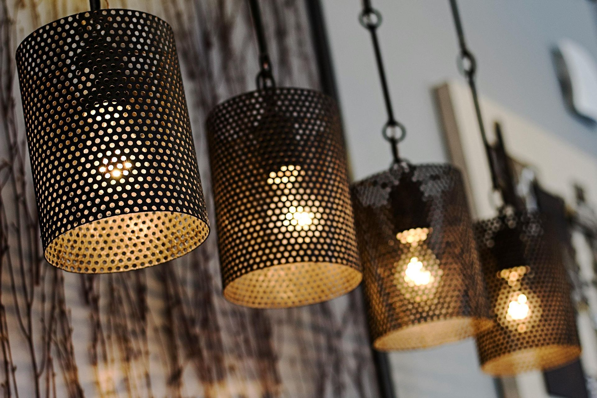 Four cylindrical pendant lights with a perforated design, hanging against a textured wall.