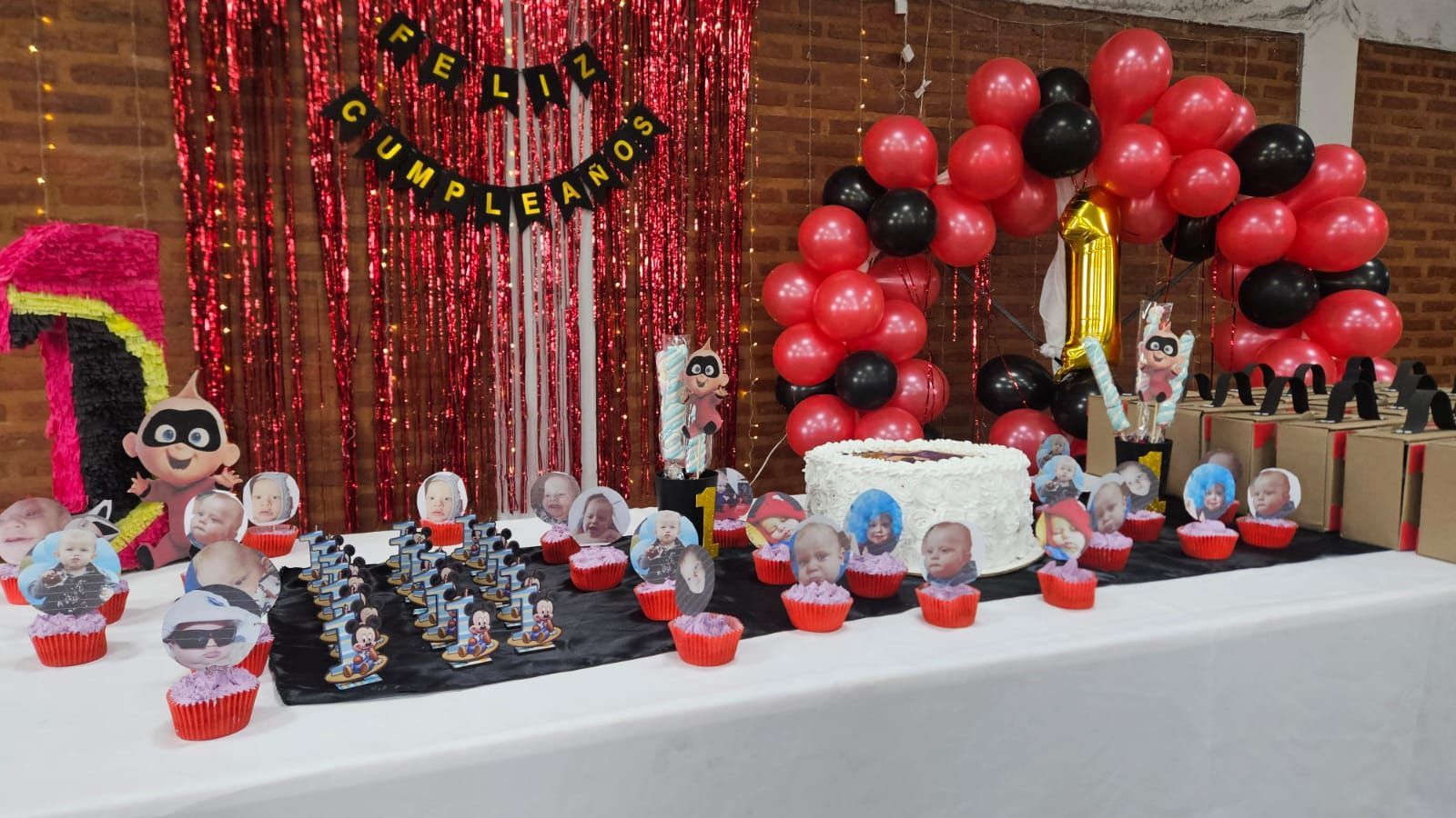Mesa de fiesta de cumpleaños con temática de Los Increíbles. Pastel, cupcakes, globos y decoraciones en rojo y negro.