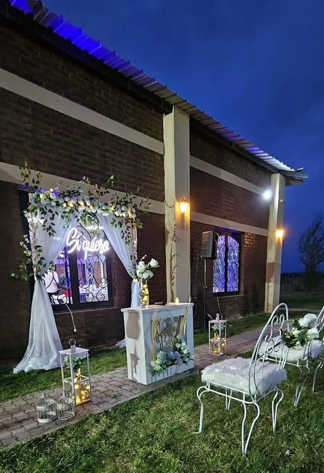 Montaje de boda al aire libre con edificio de ladrillo, decoración en blanco y azul y asientos sobre césped verde.