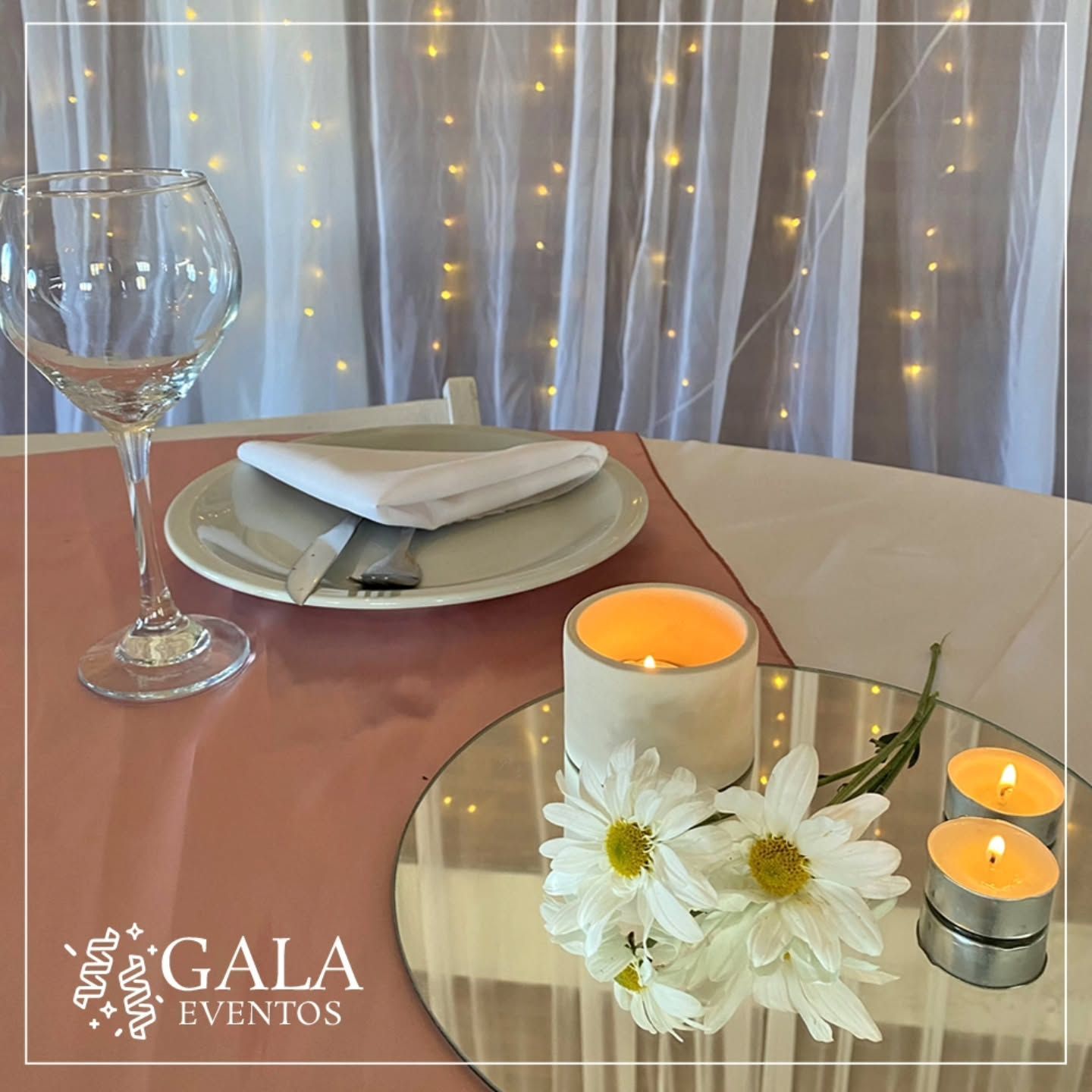 Elegante mesa con mantel rosa, copa de vino, flores y velas.