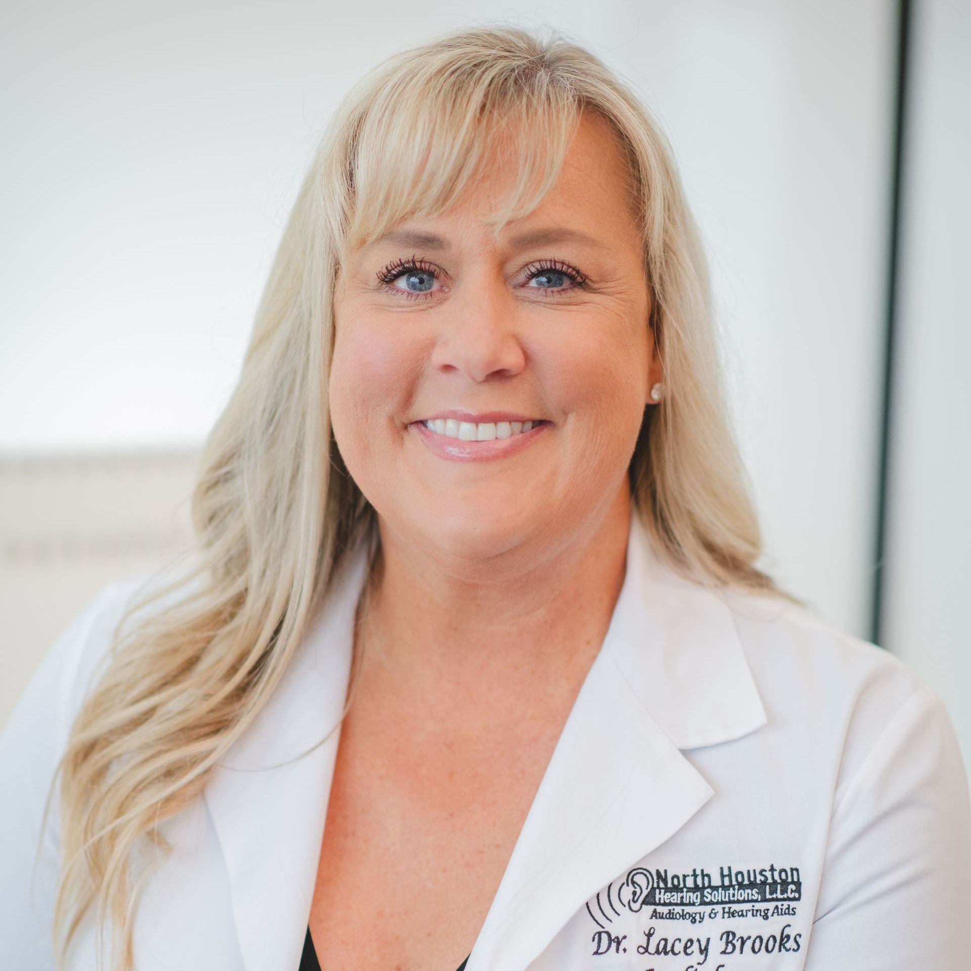 A woman wearing a white lab coat that says dr. lacey brooks audiology