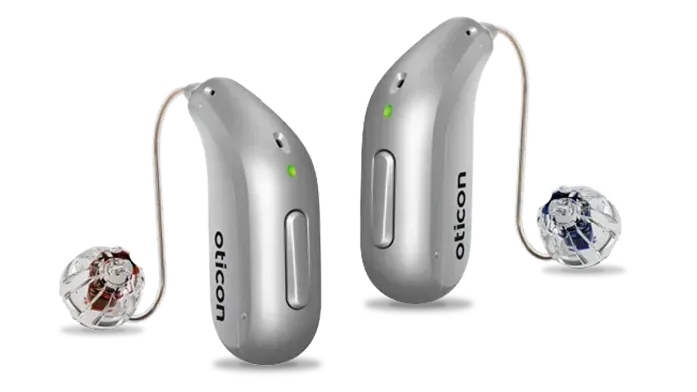 A pair of silver hearing aids made by oticon