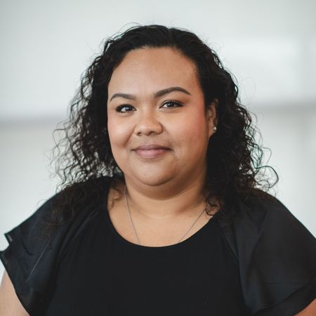 A woman with curly hair is wearing a black shirt and smiling for the camera.