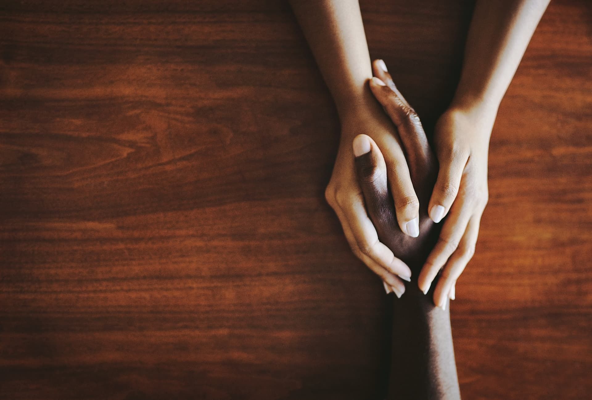 A couple of hands holding each other on a wooden table.