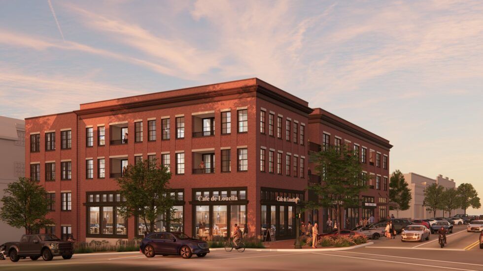 A three-story red brick building with ground-floor storefronts and upper-level residences on a street at sunset.