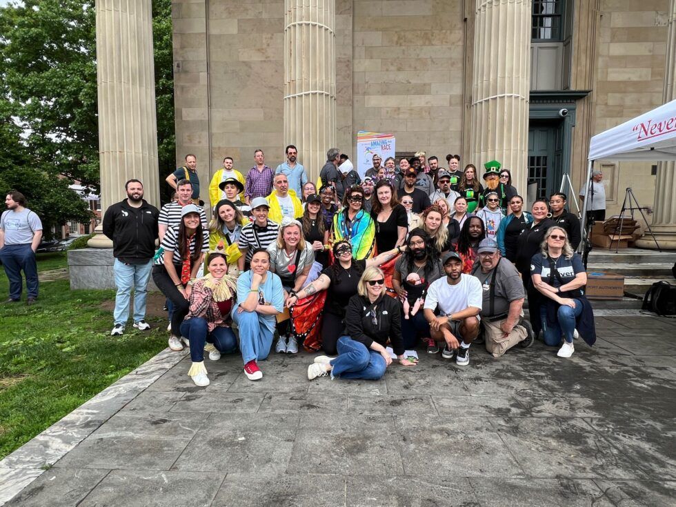 A large group of people smiling and posing for a photo in front of a building with large stone columns.