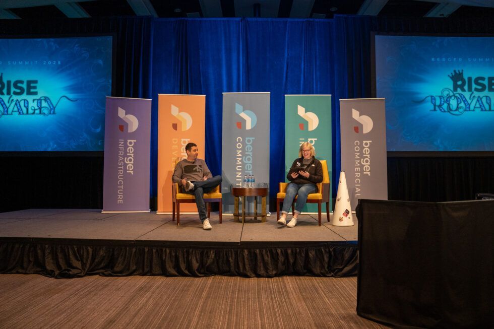 Two people sit on chairs on a stage in front of colored banners with a