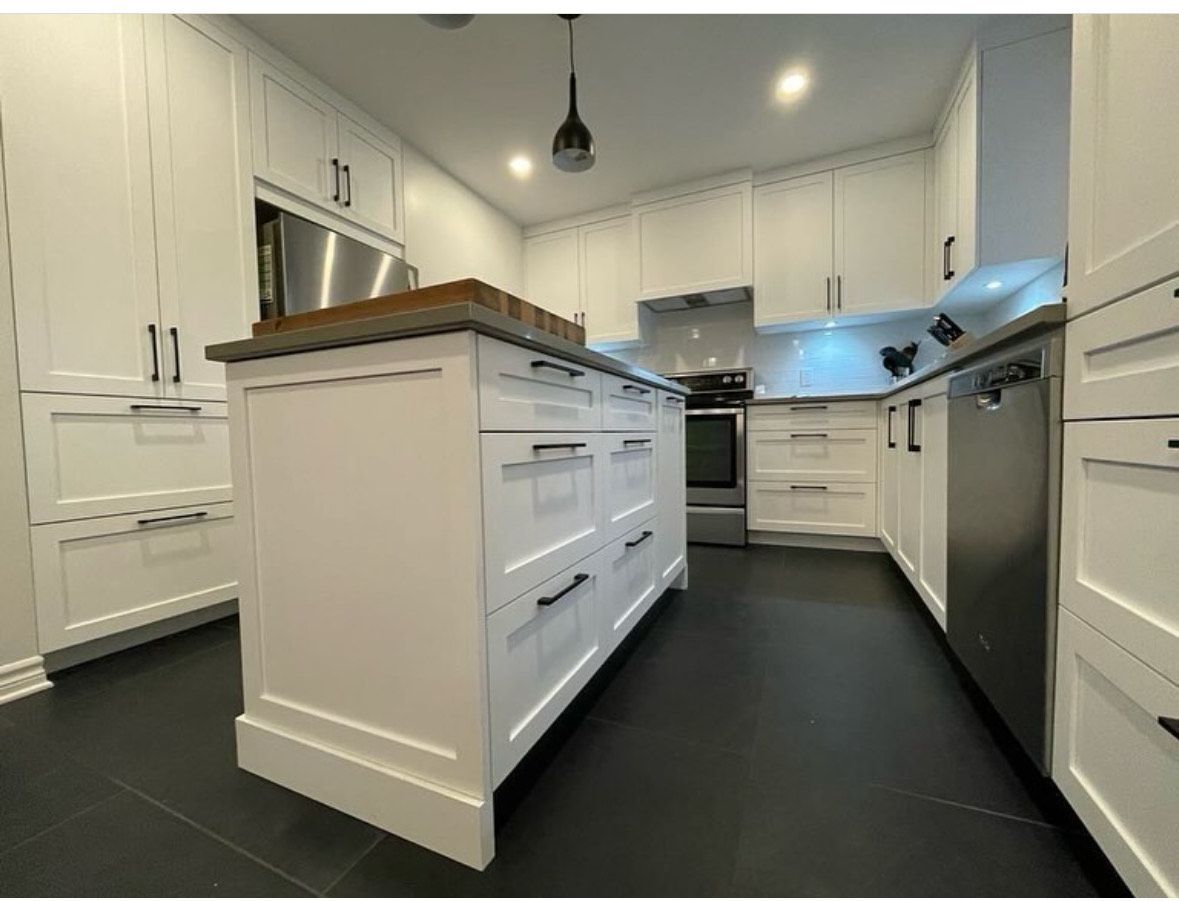 Une cuisine avec des armoires blanches et des appareils en acier inoxydable et un grand îlot au milieu.