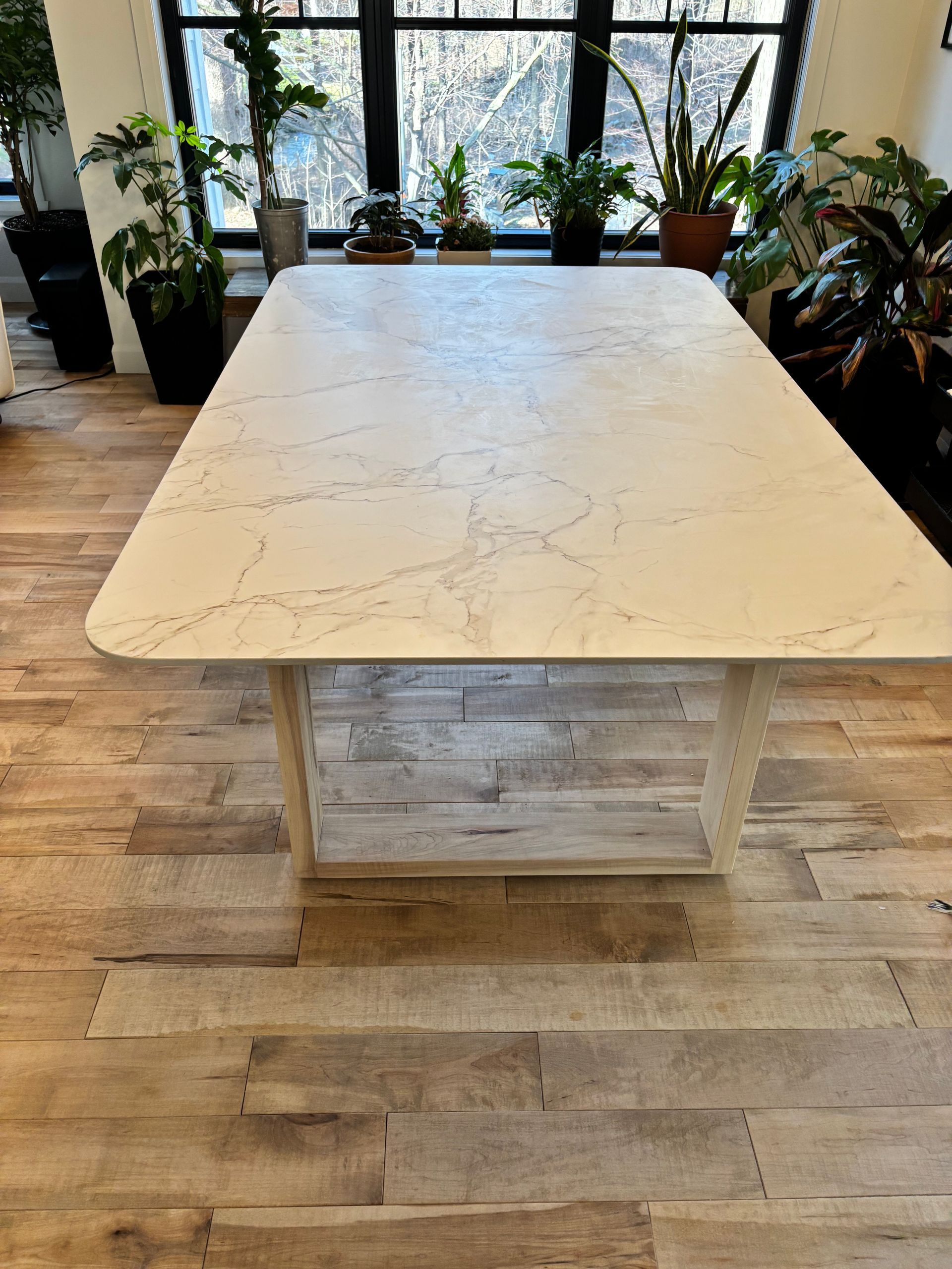Une table en marbre blanc est posée sur un plancher en bois devant une fenêtre.