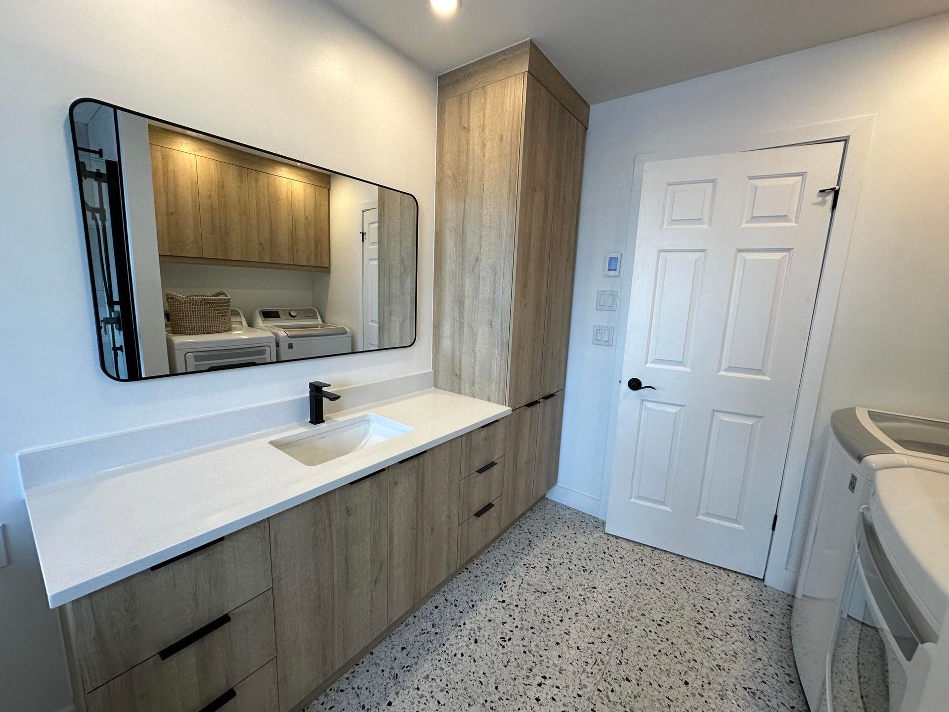 Une buanderie avec un évier, une laveuse et une sécheuse, et un grand miroir.