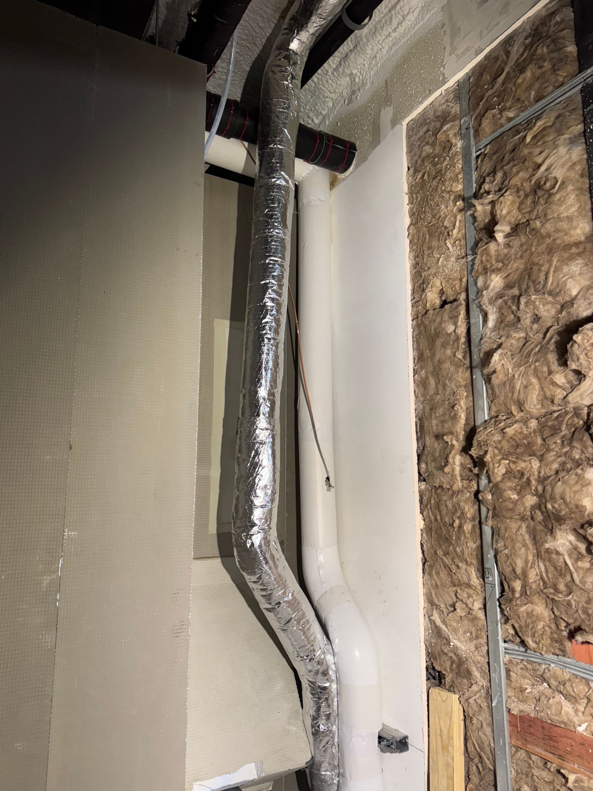 Flexible, silver ductwork runs along a wall with insulation and drywall partially installed.