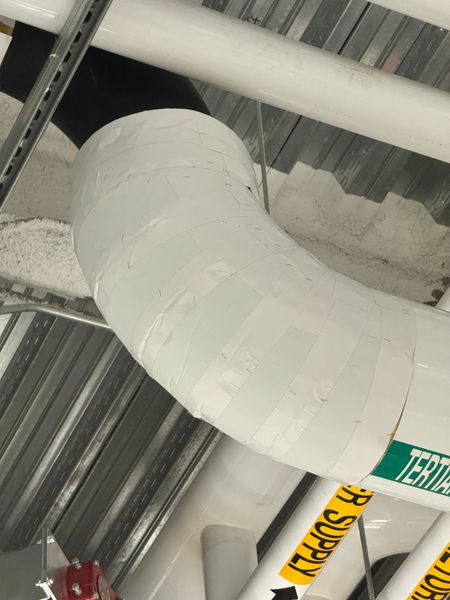White-taped curved pipe under a metal ceiling. The pipe is labeled 