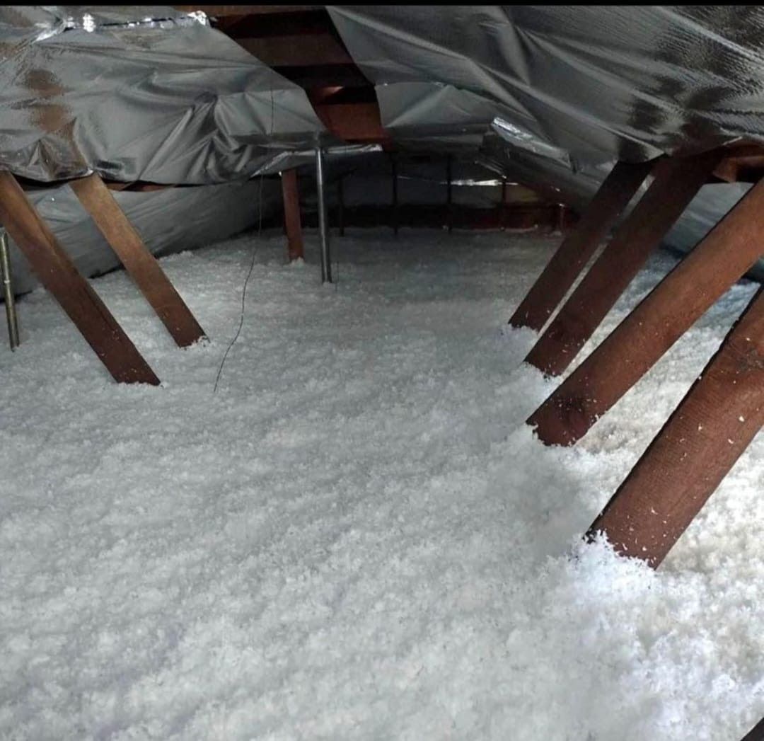 Attic filled with white insulation; wooden rafters and supports are visible. Silver reflective material lines the ceiling.