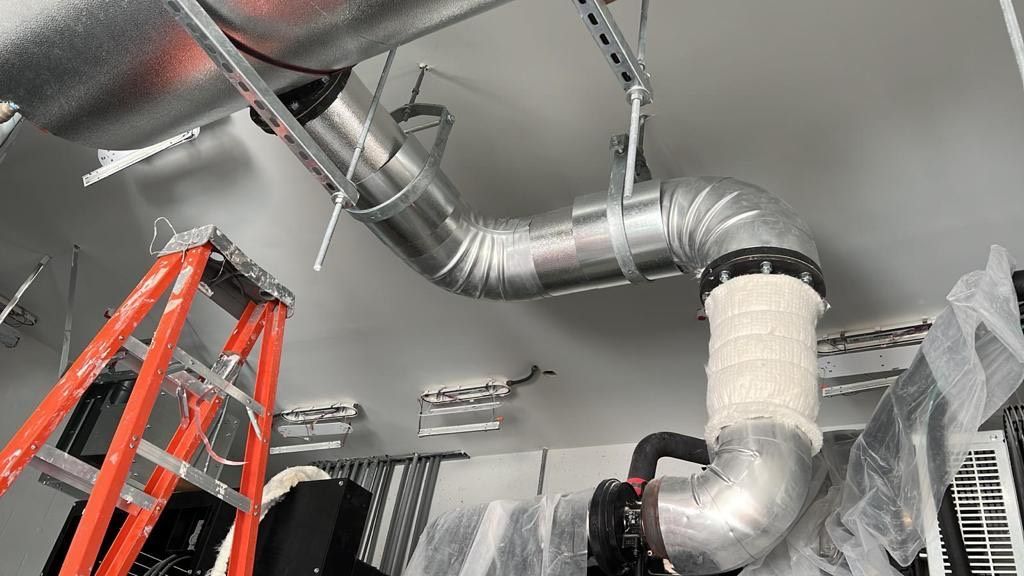 HVAC ductwork installation in a room, with ladder and insulation visible.