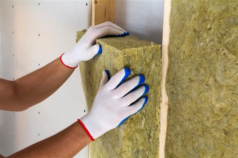 Hands in gloves installing insulation between wall studs.
