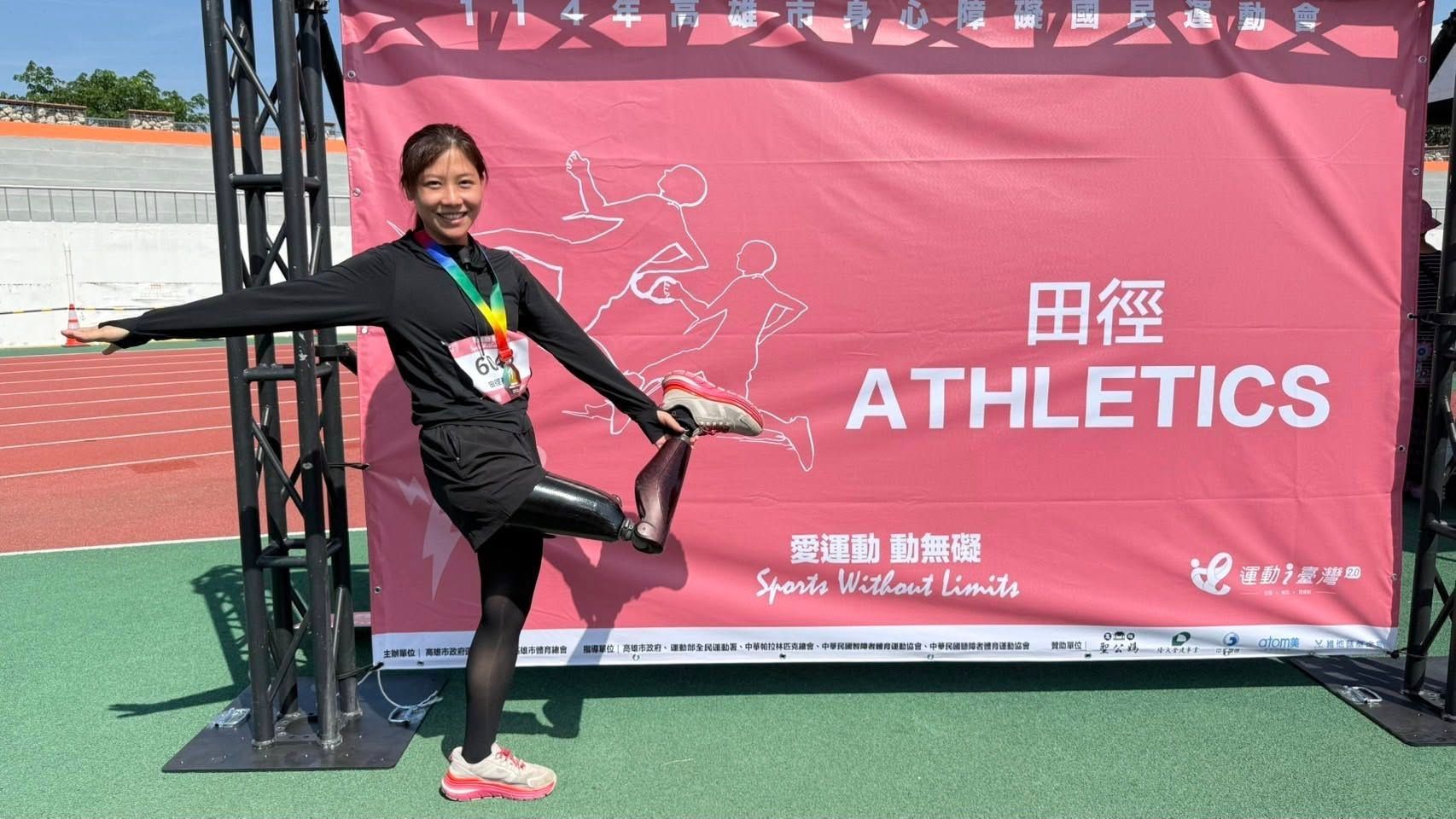 永純之友宇捷：在 114 年身障運動會田徑背板前，單腳站立展現優美平衡，穿戴深色金屬質感的膝下義肢與紅色運動鞋，脖子上掛著象徵榮譽的彩虹獎牌。