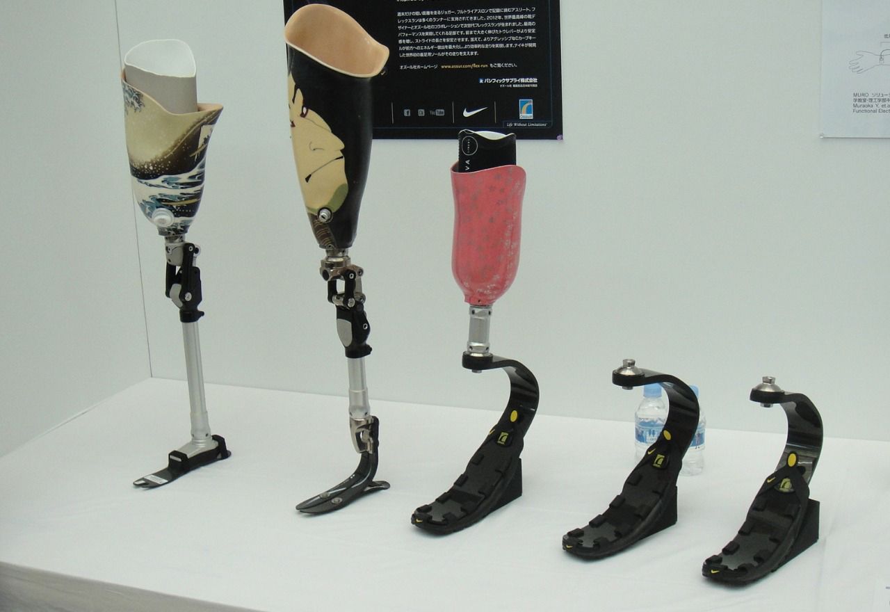 永純運動型義肢：一整排針對競技設計的義肢展示，包含具有彩繪圖騰的接受腔，以及專為跑步設計的 J 型碳纖維彈力刀鋒腳掌。