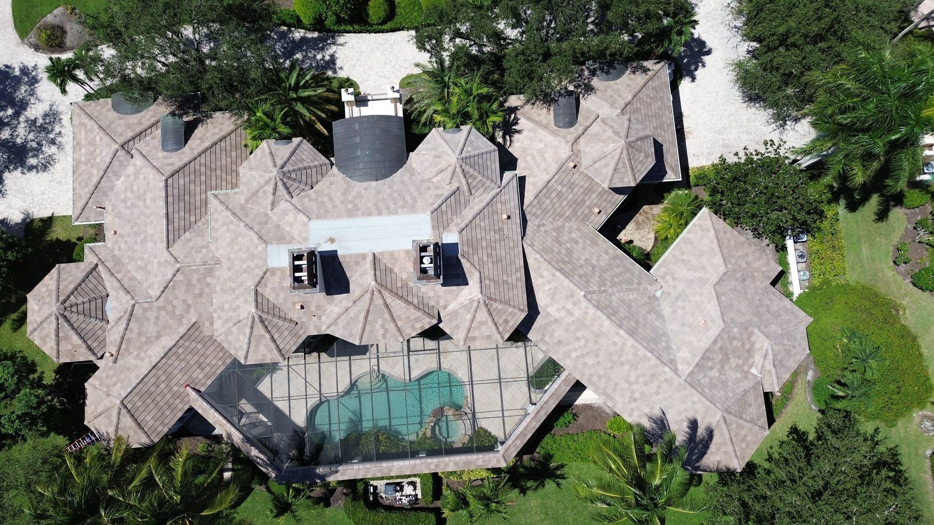 Aerial view of a large house with a complex roof, a swimming pool, and surrounding greenery.