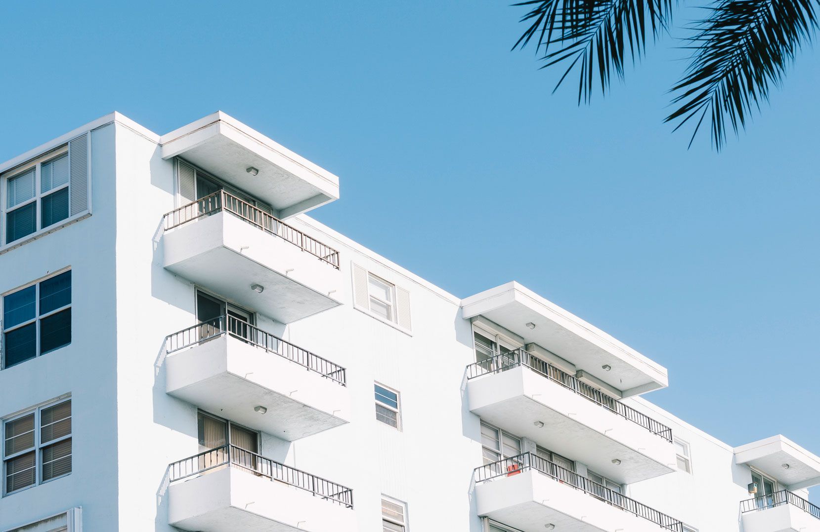 A white apartment building with balconies and a palm tree in the background.