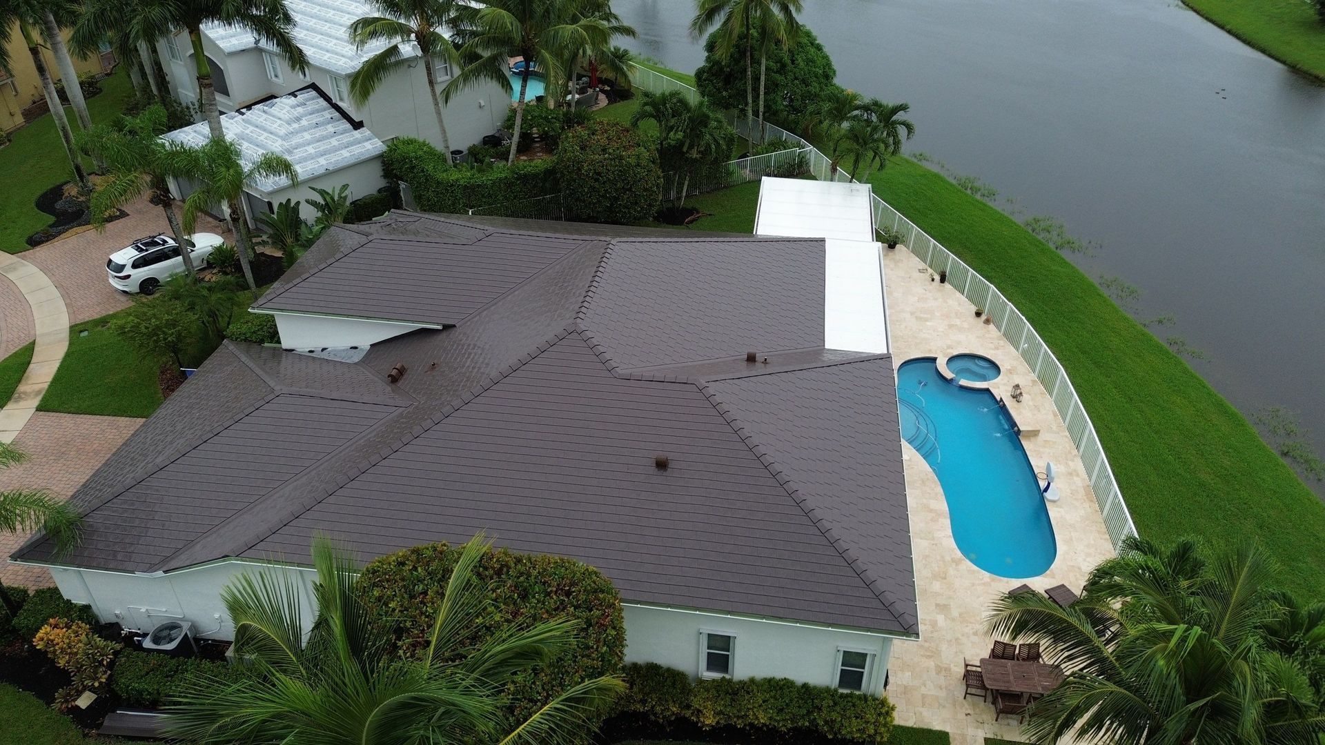 An aerial view of a white house with a brown roof, a pool, and a lake.