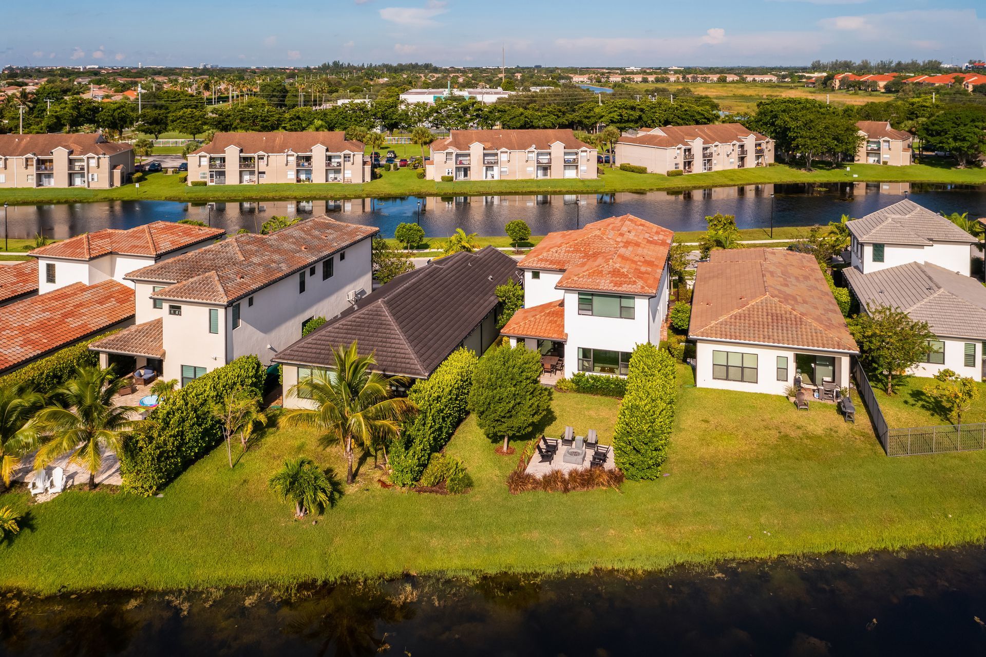 Aerial view of waterfront homes with different colored roofs, green lawns, and a lake in front.