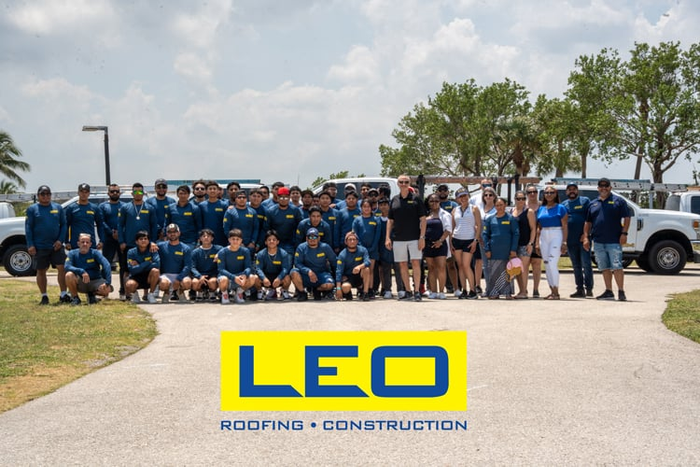 Group photo of LEO Roofing & Construction employees in uniform, posing on a paved area, logo in the foreground.