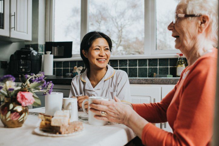 Woman with older woman in kitchen, smiling while holding mugs.