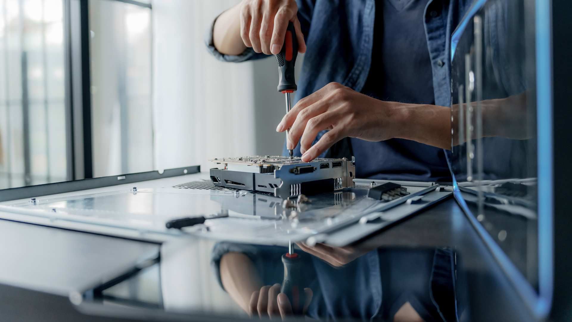 Hands assembling a small electronic device on a reflective workbench in a modern lab.