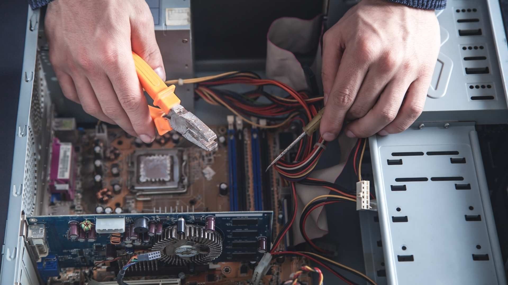 Hands using pliers to work inside an open desktop computer case with exposed motherboard and cables