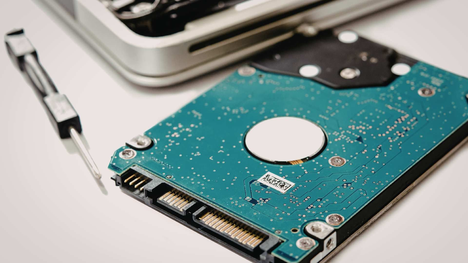 Open hard disk drive with teal circuit board and exposed connector on a white surface