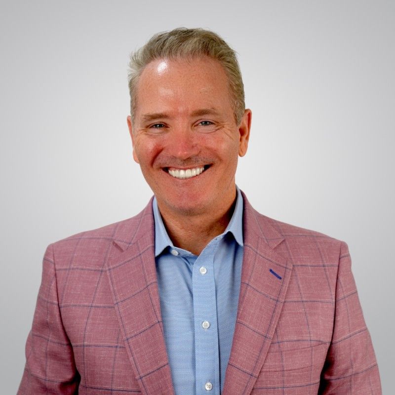 Smiling man in a pink blazer and blue shirt against a light gray background