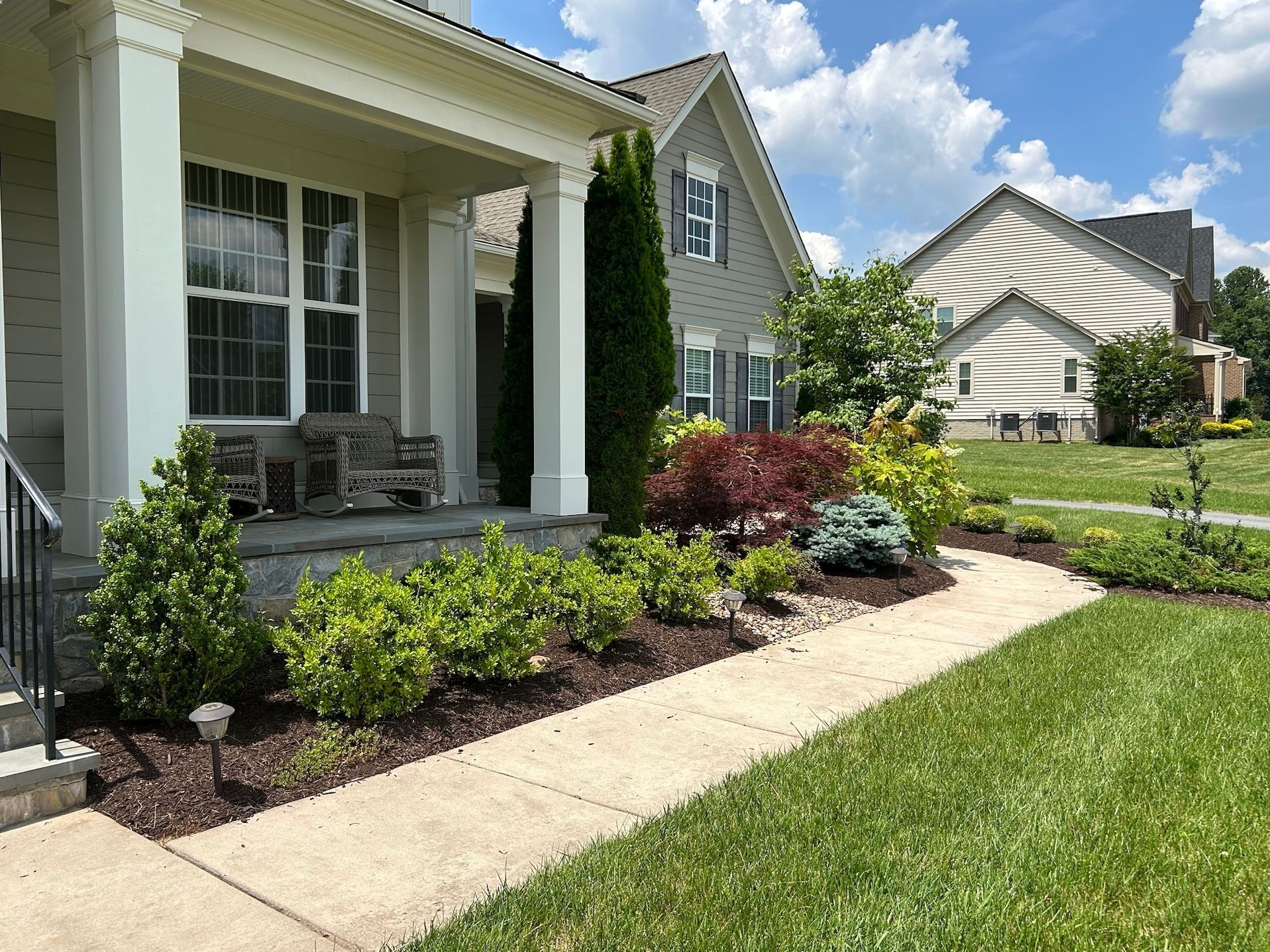 Front porch with white columns, garden beds, and a curved walkway beside a suburban house