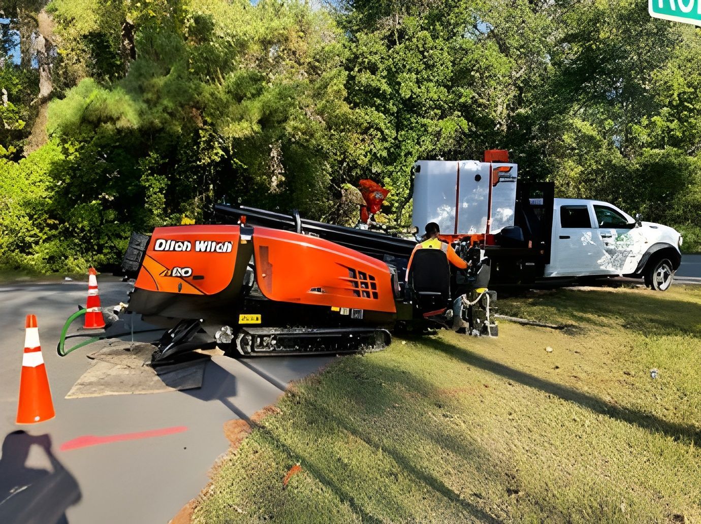 Tow truck recovering orange utility machine from grassy roadside near traffic cones