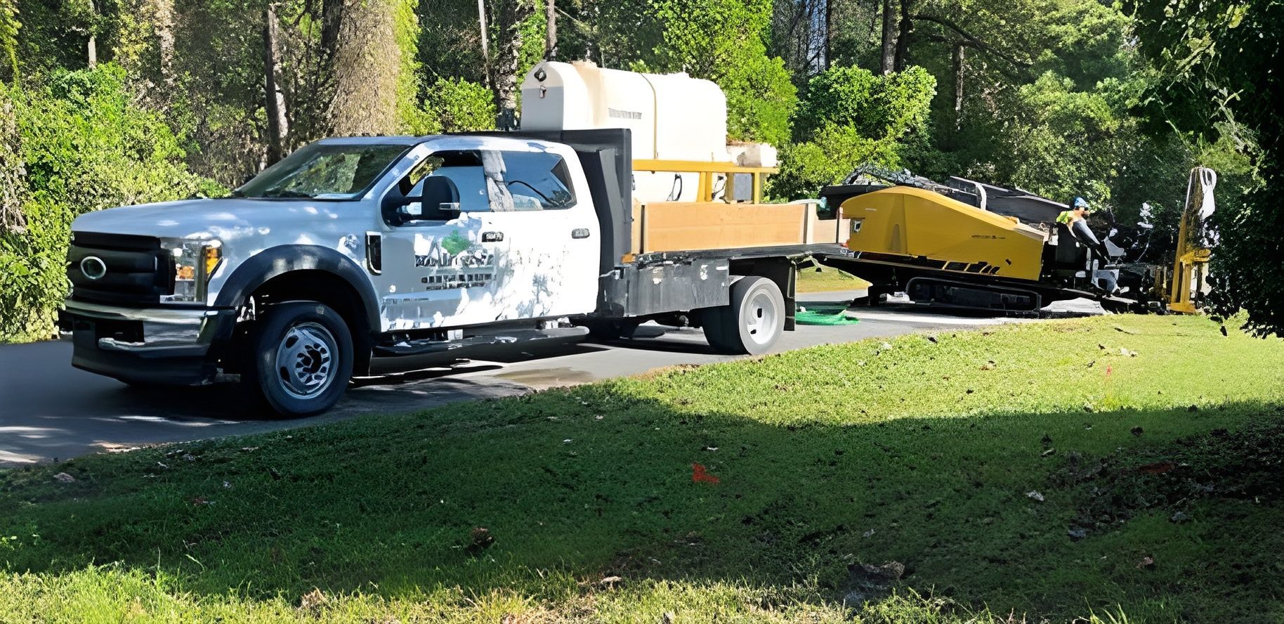 White utility truck with equipment and trailer parked on grass in a wooded area