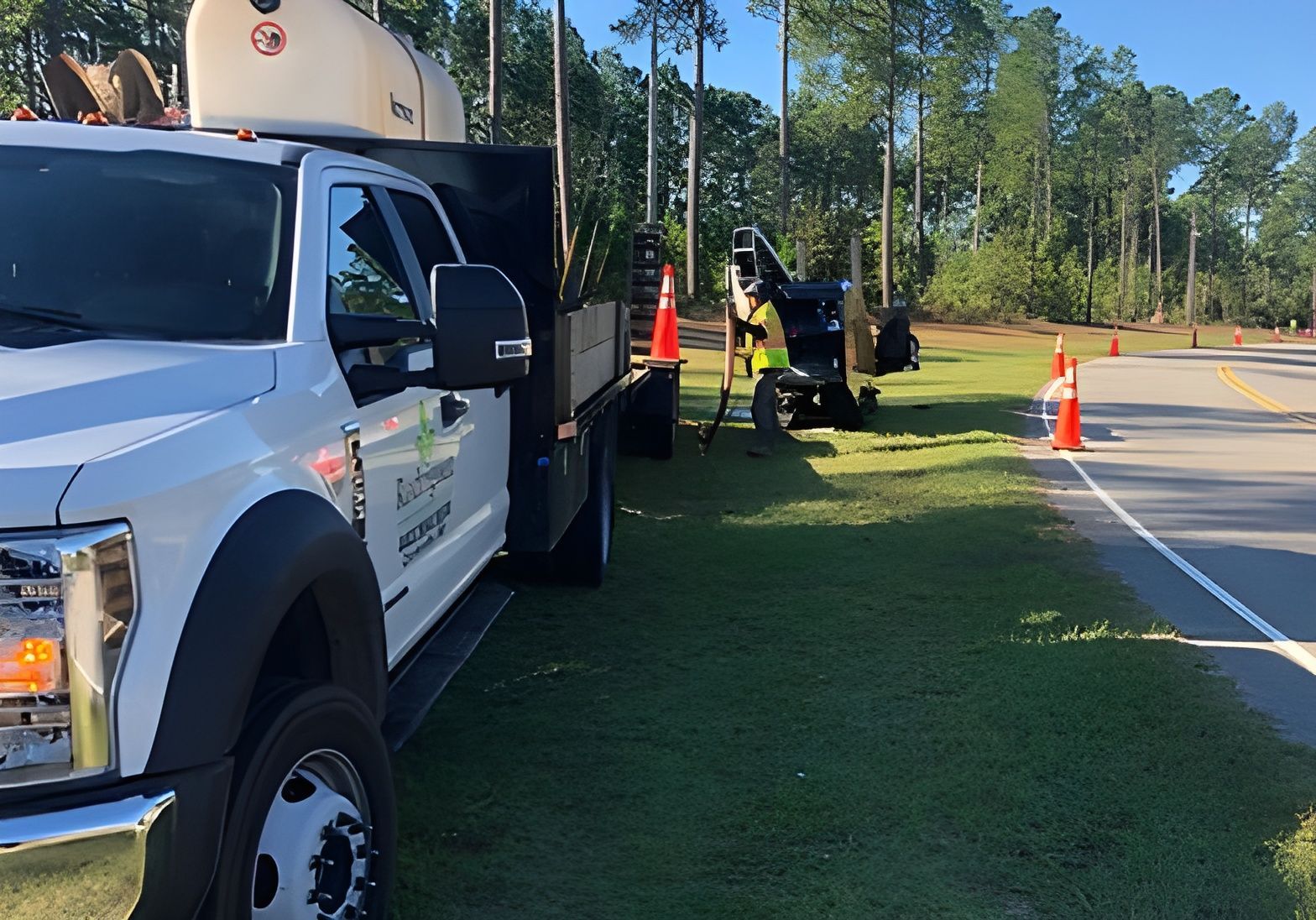 White utility truck and roadside workers with cones on a sunny highway shoulder