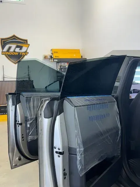 The interior door panel of a car is covered in protective plastic film inside an automotive shop.