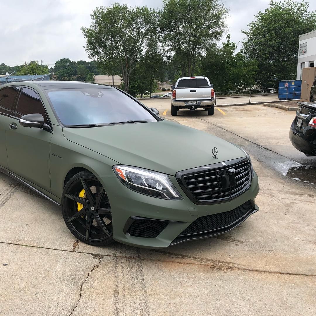 A matte army green Mercedes-Benz sedan with black wheels and bright yellow brake calipers parked in a paved lot.