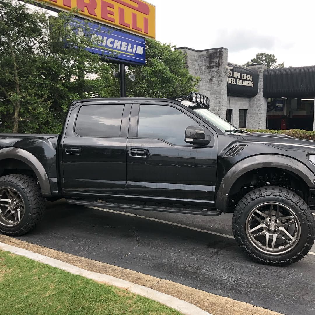 A black lifted pickup truck with custom wheels parked in front of a building with tire brand signage.
