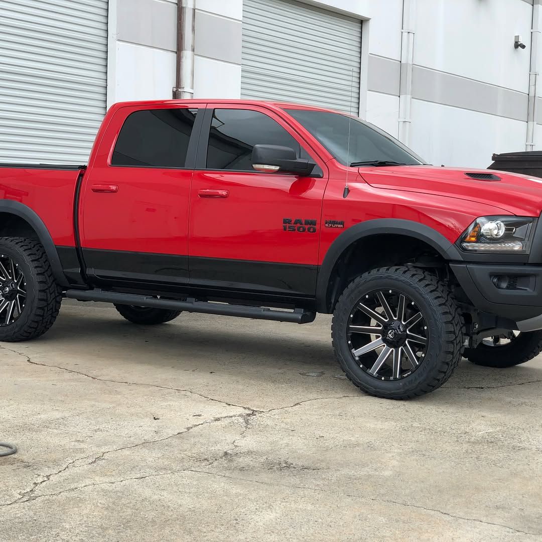 A red Ram pickup truck with black trim and custom black and silver wheels parked on concrete in front of a white building.