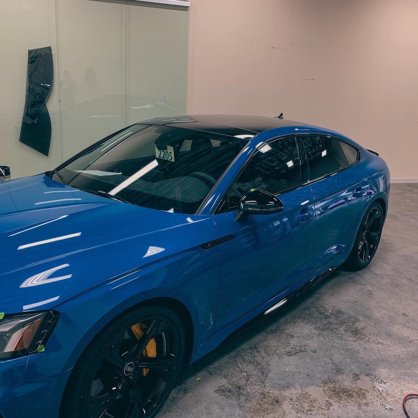 A bright blue sports sedan with black wheels and a contrasting black roof parked inside a garage.