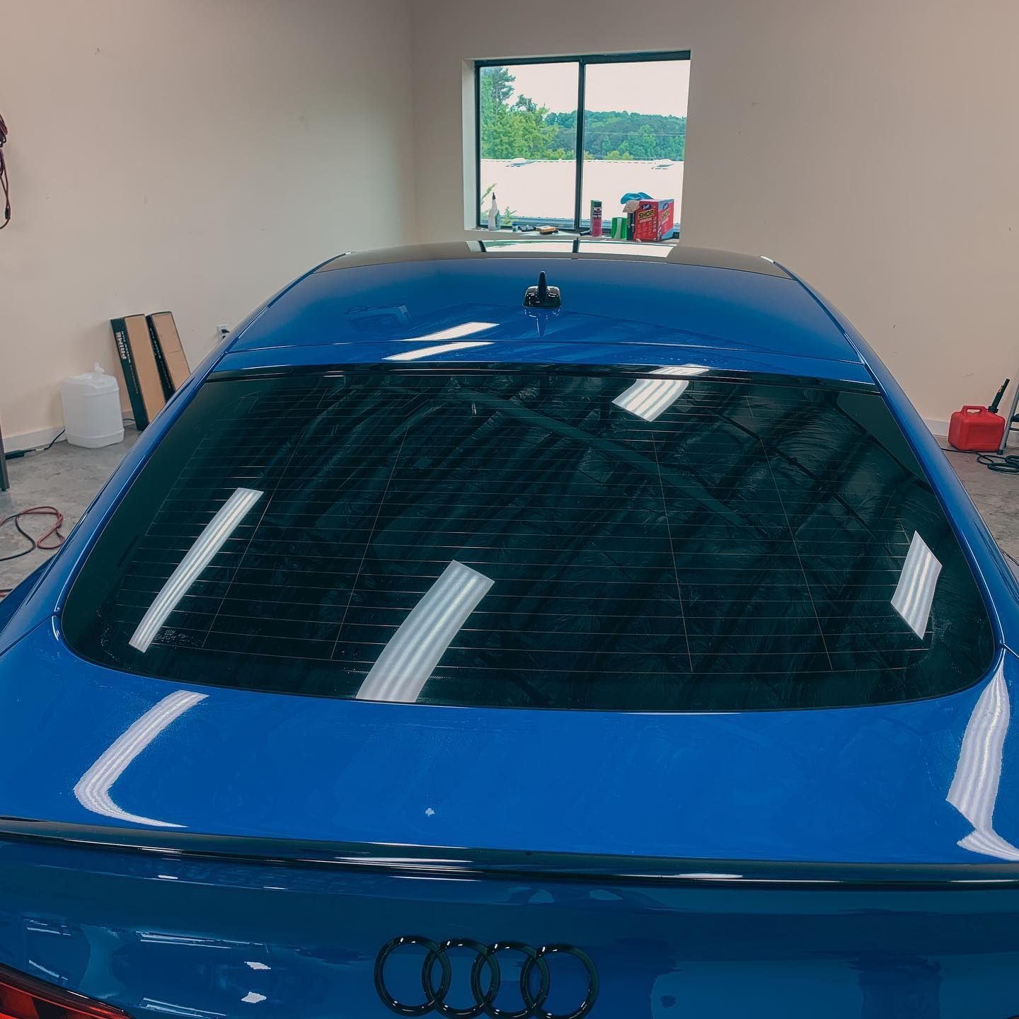 A close-up view of the rear window and trunk of a bright blue Audi car, parked inside a garage.