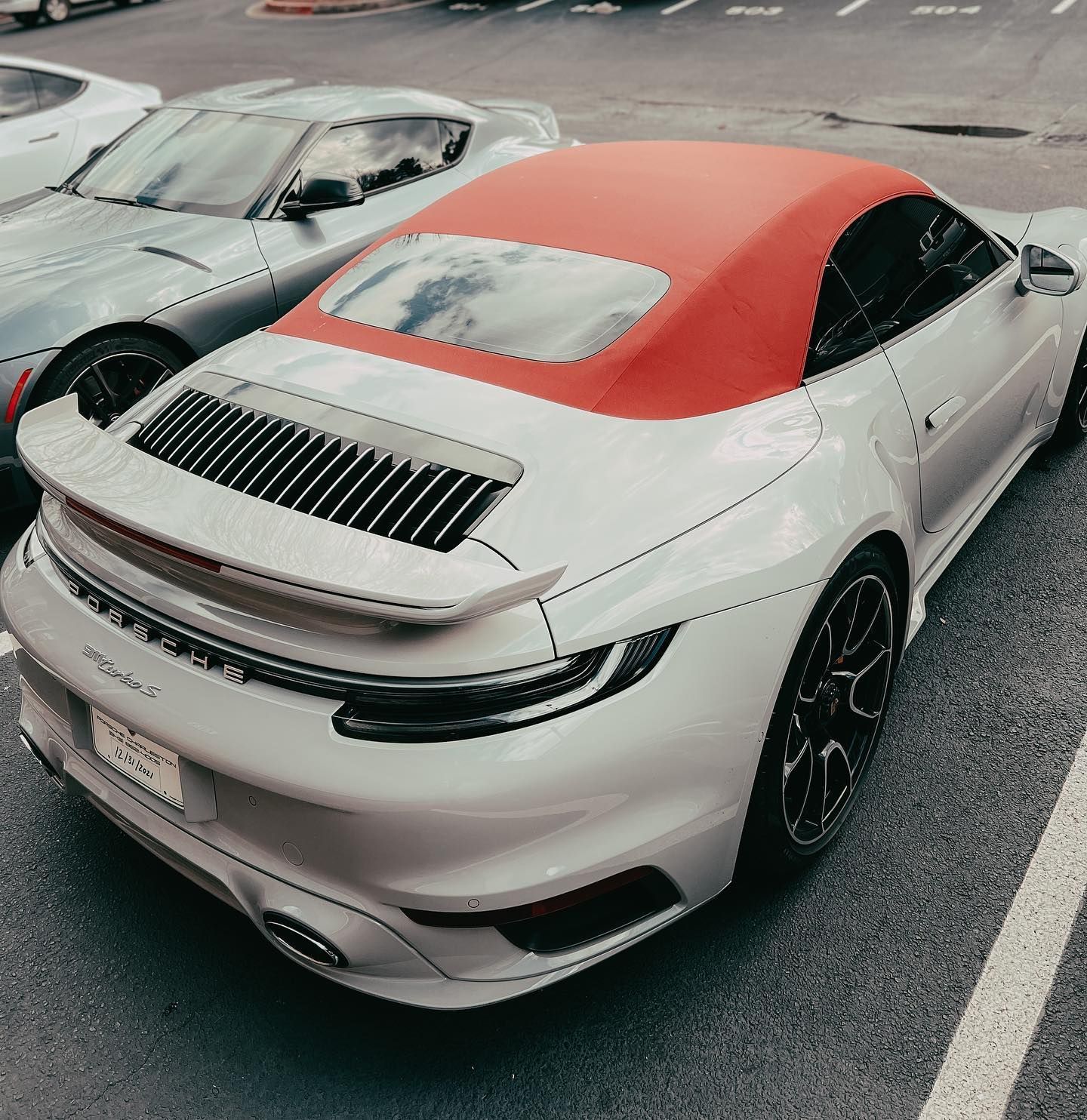 A white Porsche convertible with a red fabric roof parked in an asphalt lot next to a gray car.