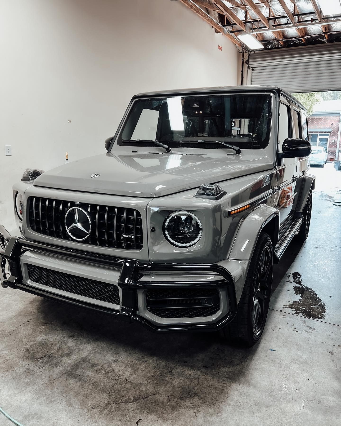 A grey Mercedes-Benz G-Class SUV parked inside a garage with a black front brush guard and dark wheels.